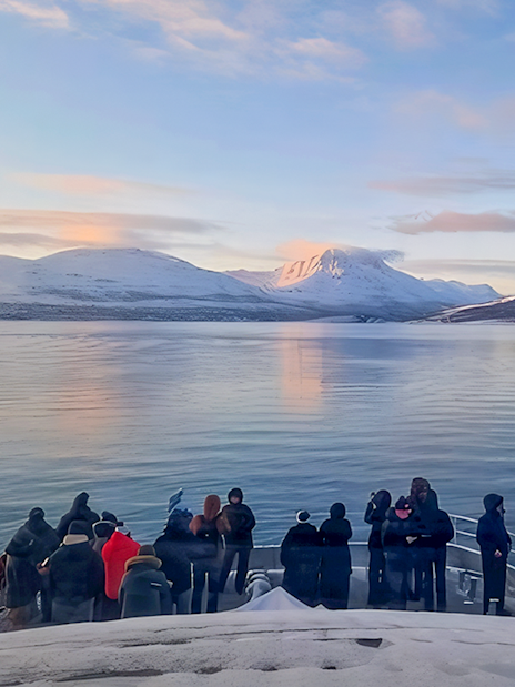 Guests on a boat watching for whales in Tromso with snowy mountains in the background.