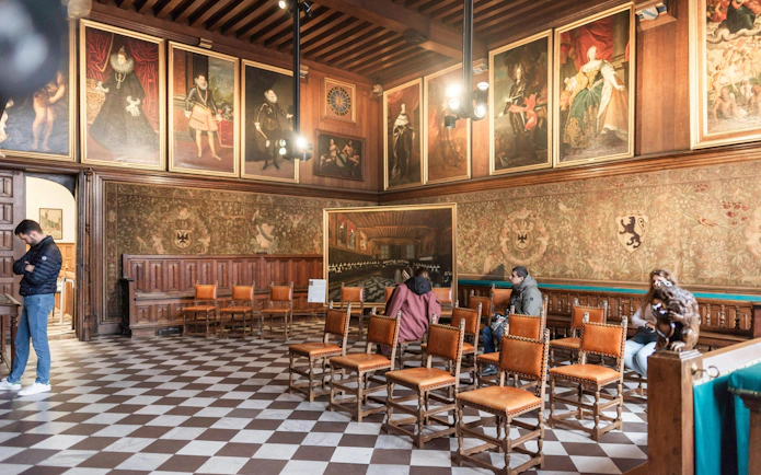 Brugse Vrije interior with historical paintings and visitors in Bruges, Belgium.