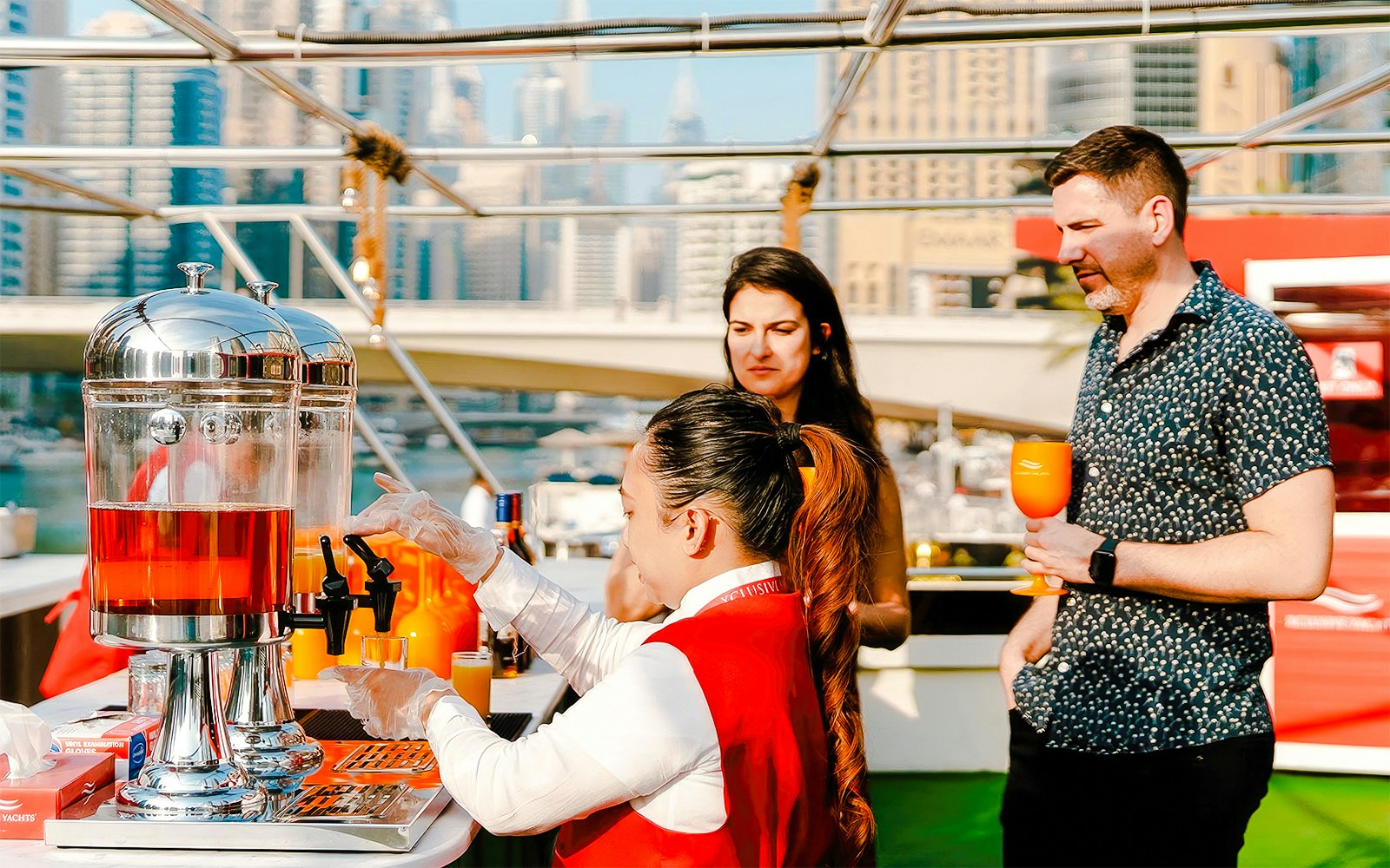 Visitors on a Dubai Marina sunset cruise enjoying drinks with city skyline in the background.