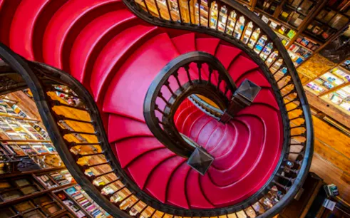 Curved red staircase inside Livraria Lello, Porto.