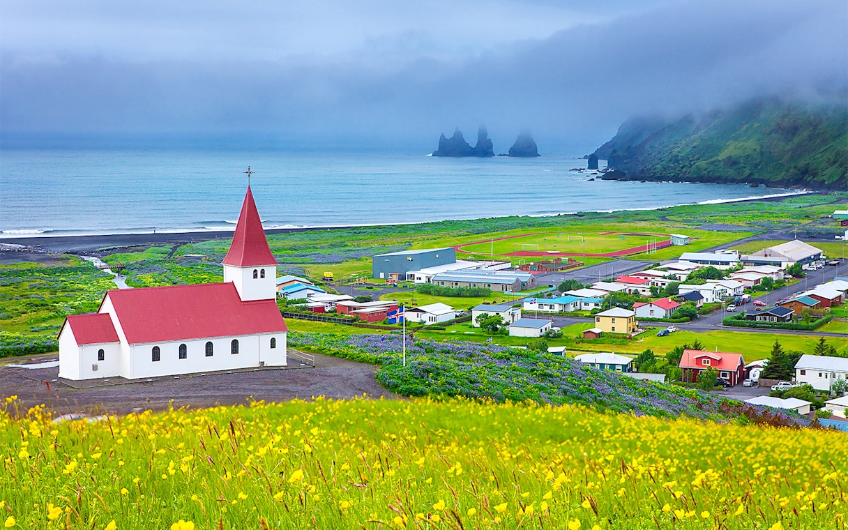 Church with red roof in Vik, Iceland, overlooking ocean and Reynisdrangar sea stacks.
