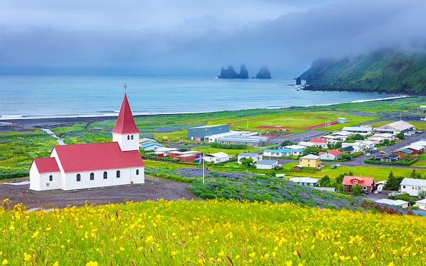Church with red roof in Vik, Iceland, overlooking ocean and Reynisdrangar sea stacks.