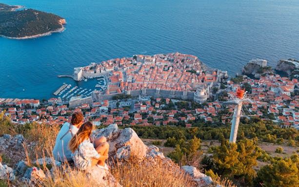 Young couple overlooking Dubrovnik from Fort Imperial, Croatia, with city walls and Adriatic Sea.