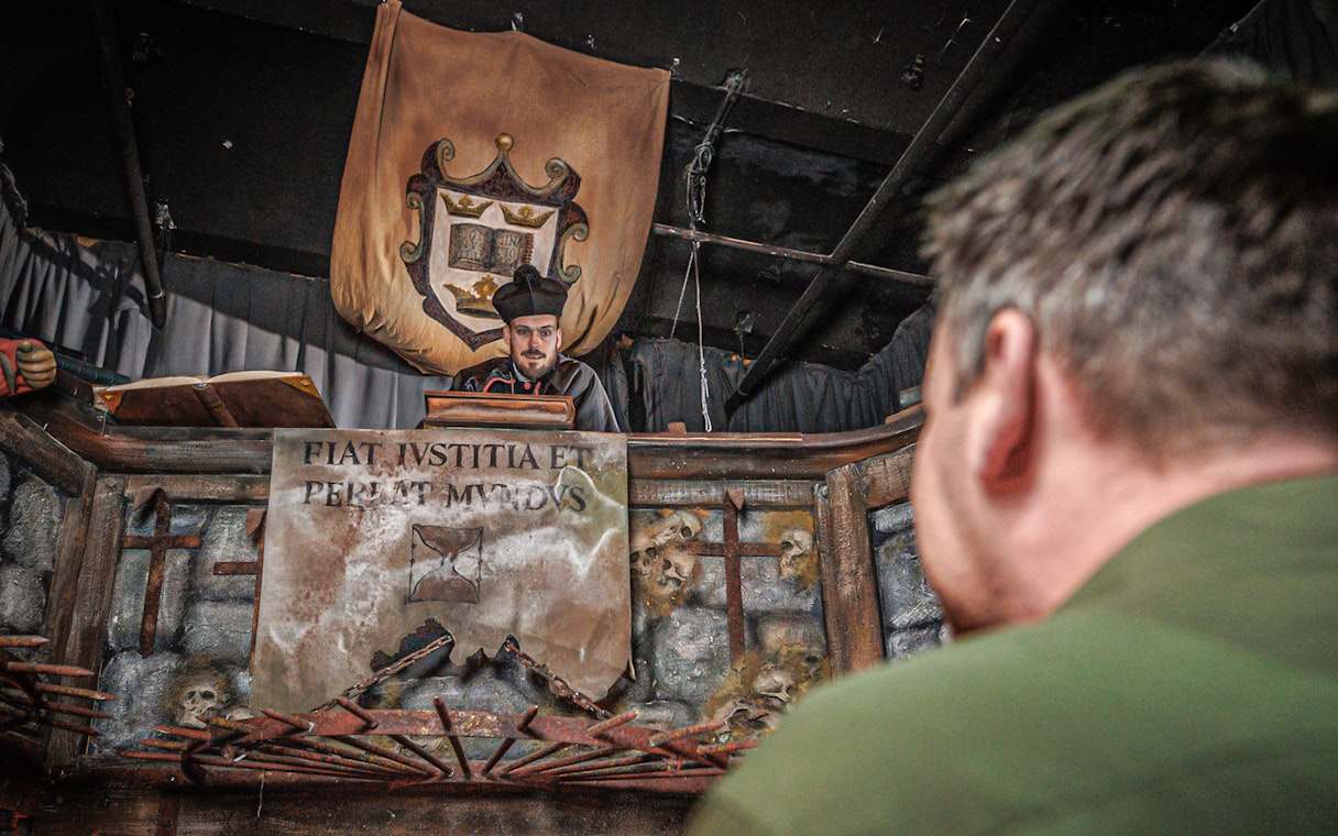 Judge performing act inside Hamburg Dungeon with medieval decor and audience member.
