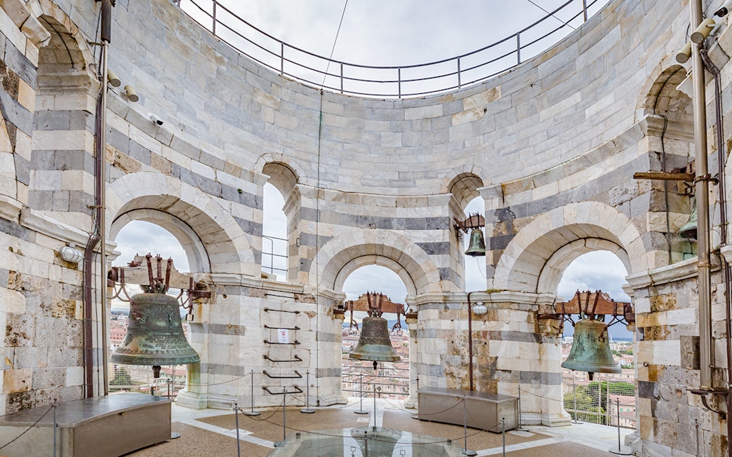 Bells at the top of the Leaning Tower of Pisa, Italy, with city view through arches.