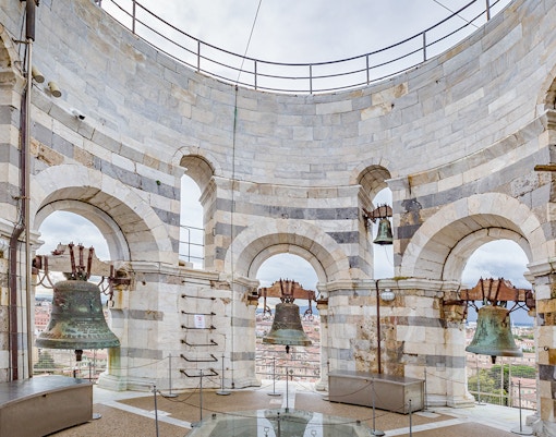 Bells at the top of the Leaning Tower of Pisa, Italy, with city view through arches.