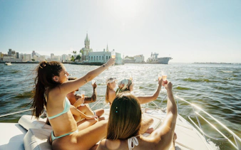 Tourists enjoying a boat ride in Guanabara Bay, Rio de Janeiro, with cityscape and historic building in view.
