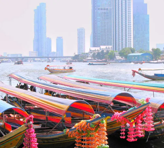 Colorful long-tail boats on a Bangkok canal with city skyline in the background.