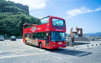 Red double-decker tour bus in San Sebastian near a modern sculpture and scenic view.