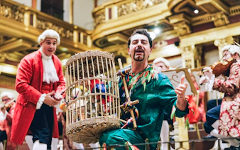 Musicians in period costumes performing at a Mozart Orchestra Concert with a birdcage prop.