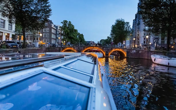 Evening canal cruise in Amsterdam with illuminated bridge reflections.