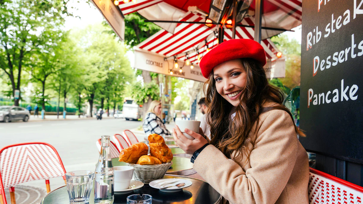 Young woman enjoying coffee at a Parisian café with croissants on the table.