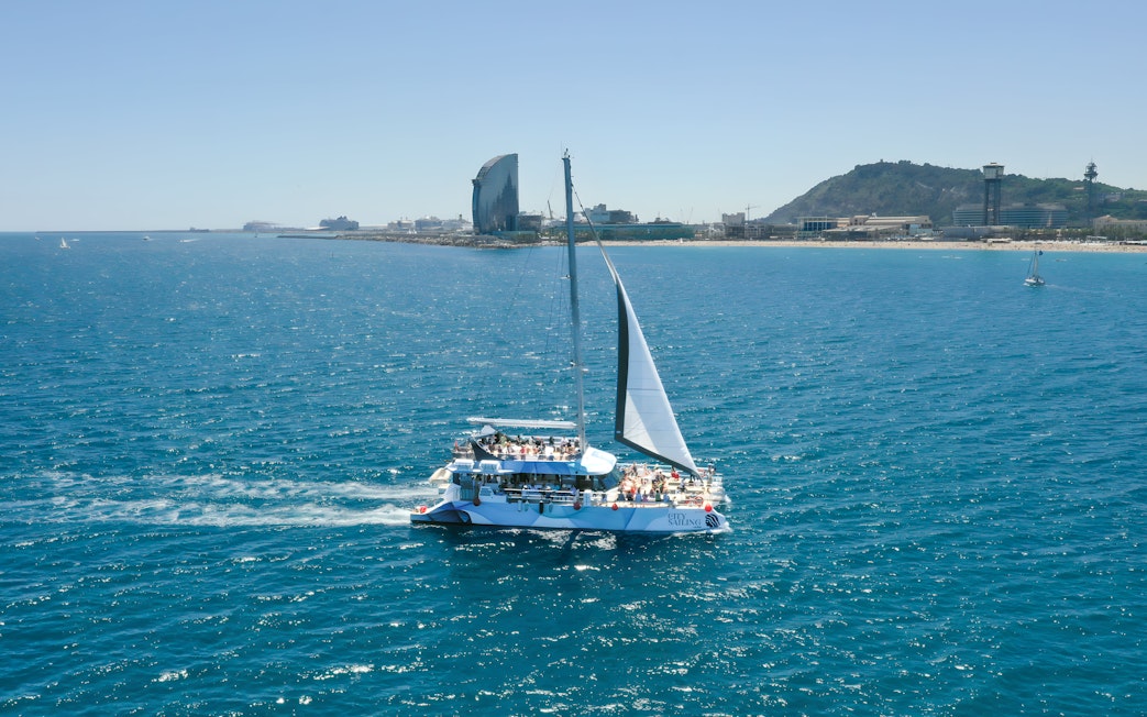 Tourists on an eco catamaran cruise near Barcelona coastline during hop-on hop-off bus tour.