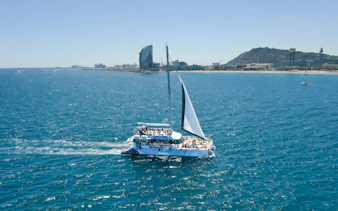 Tourists on an eco catamaran cruise near Barcelona coastline during hop-on hop-off bus tour.