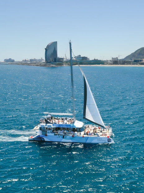 Tourists on an eco catamaran cruise near Barcelona coastline during hop-on hop-off bus tour.