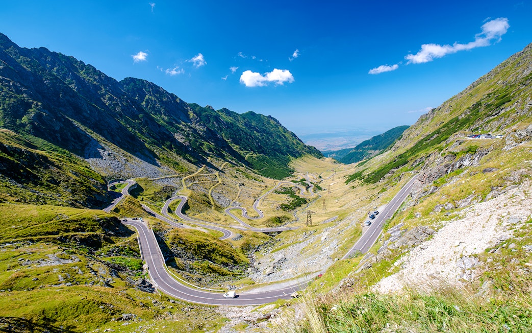 Winding Transfagarasan mountain road in Romania with cars and scenic valley view.