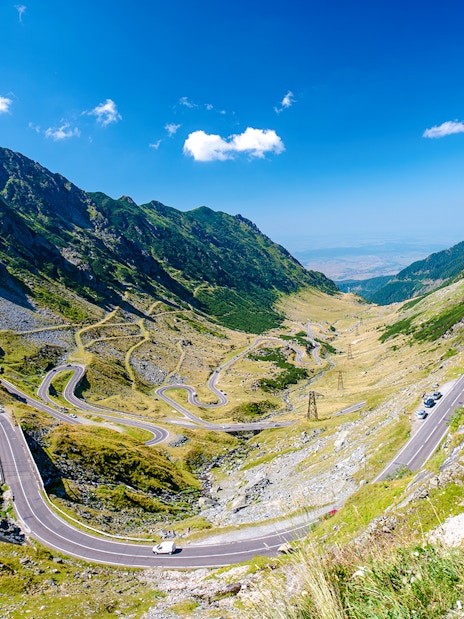 Winding Transfagarasan mountain road in Romania with cars and scenic valley view.
