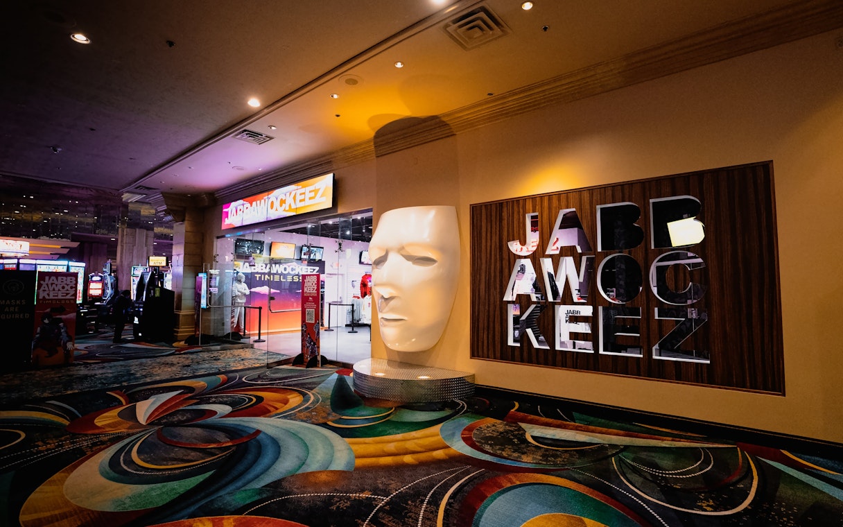 Entrance to Jabbawockeez show in Las Vegas with large mask sculpture and colorful carpet.