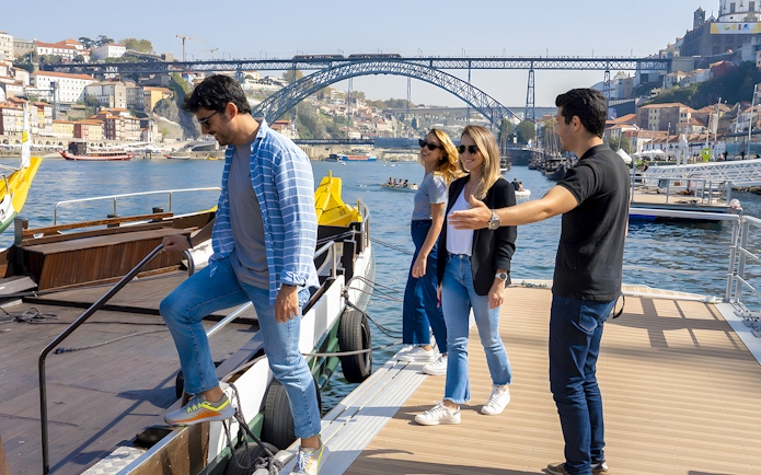 Tourists boarding a cruise with a guide at Porto walking tour, Dom Luís I Bridge in background.