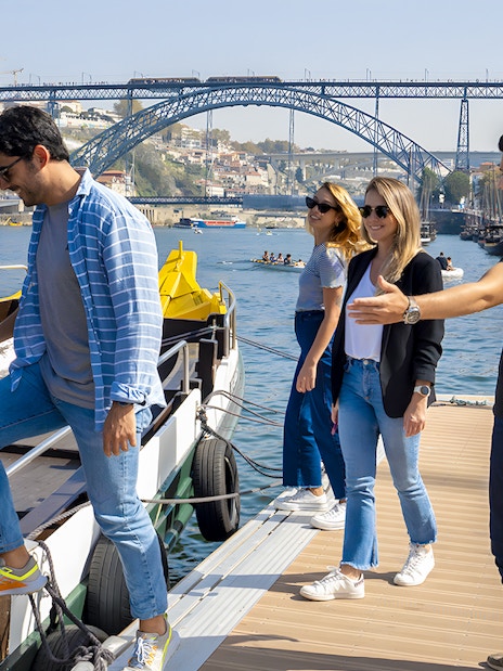Tourists boarding a cruise with a guide at Porto walking tour, Dom Luís I Bridge in background.