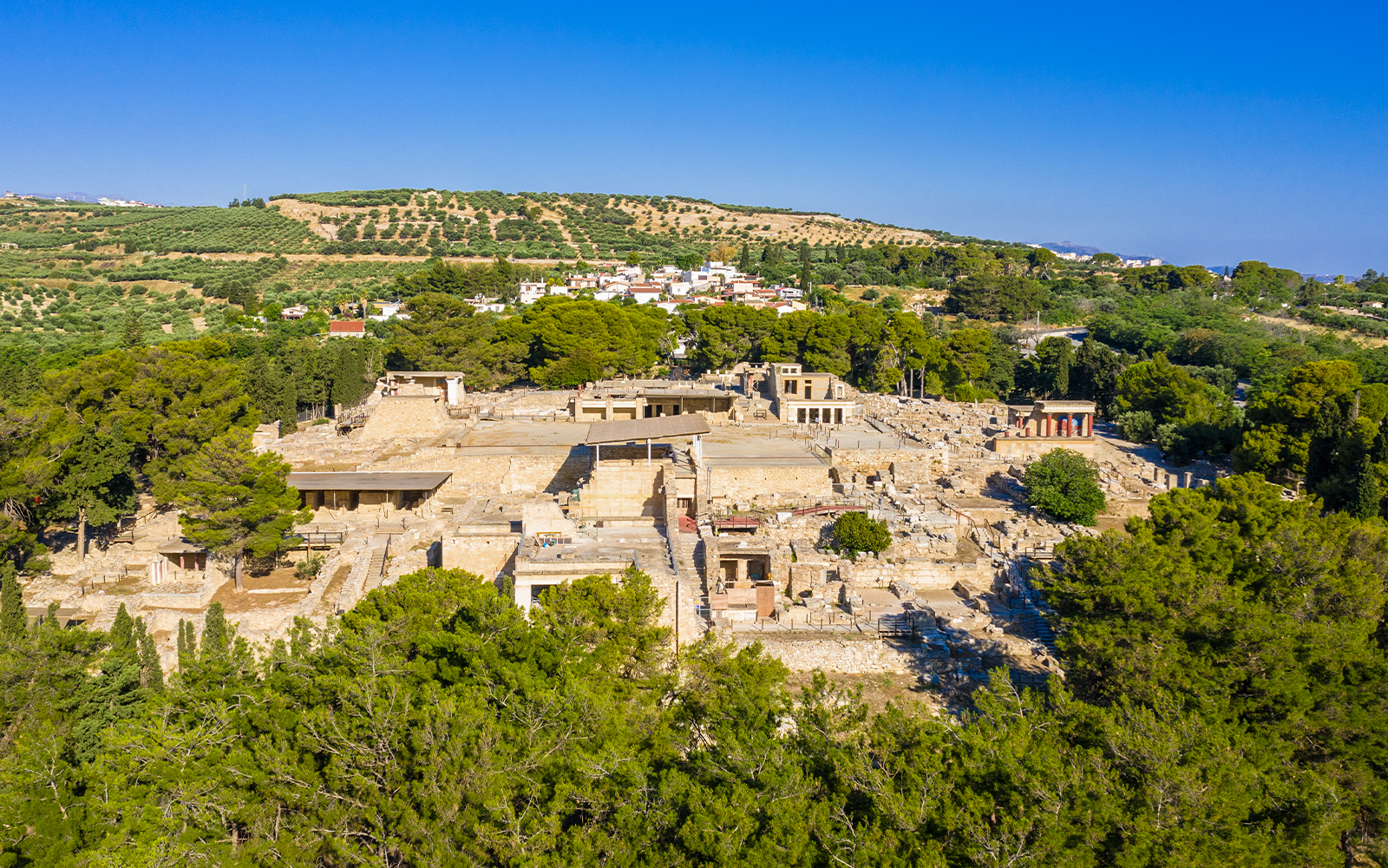 Knossos Palace ruins surrounded by lush greenery, Crete, Greece.
