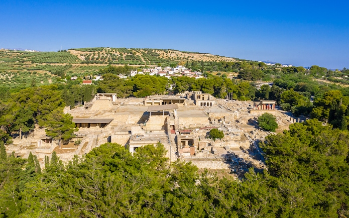 Knossos Palace ruins surrounded by lush greenery, Crete, Greece.