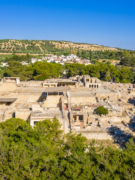 Knossos Palace ruins surrounded by lush greenery, Crete, Greece.