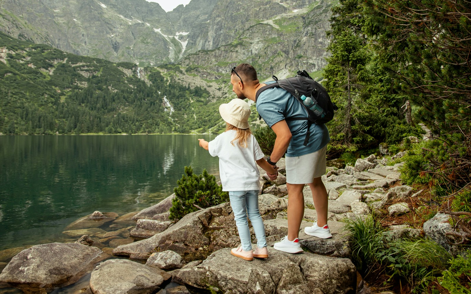 Father and child pointing at Morskie Oko lake in Zakopane, surrounded by mountains.
