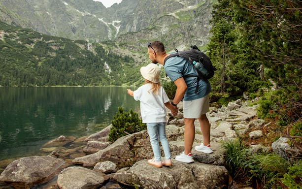 Father and child pointing at Morskie Oko lake in Zakopane, surrounded by mountains.