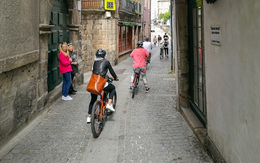 Cyclists riding through narrow cobblestone streets in Porto.