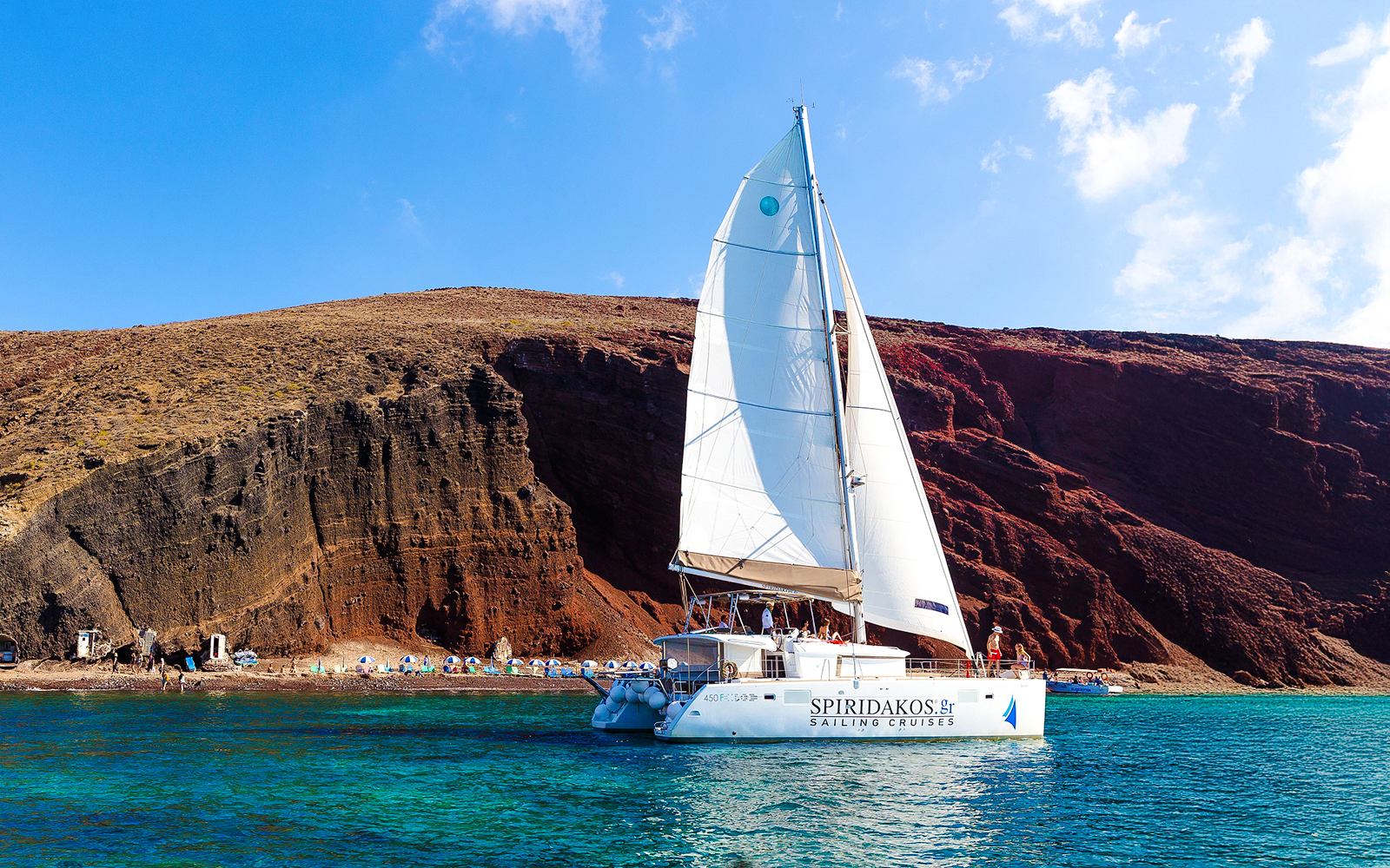 Catamaran sailing near the red cliffs of Santorini, Greece.