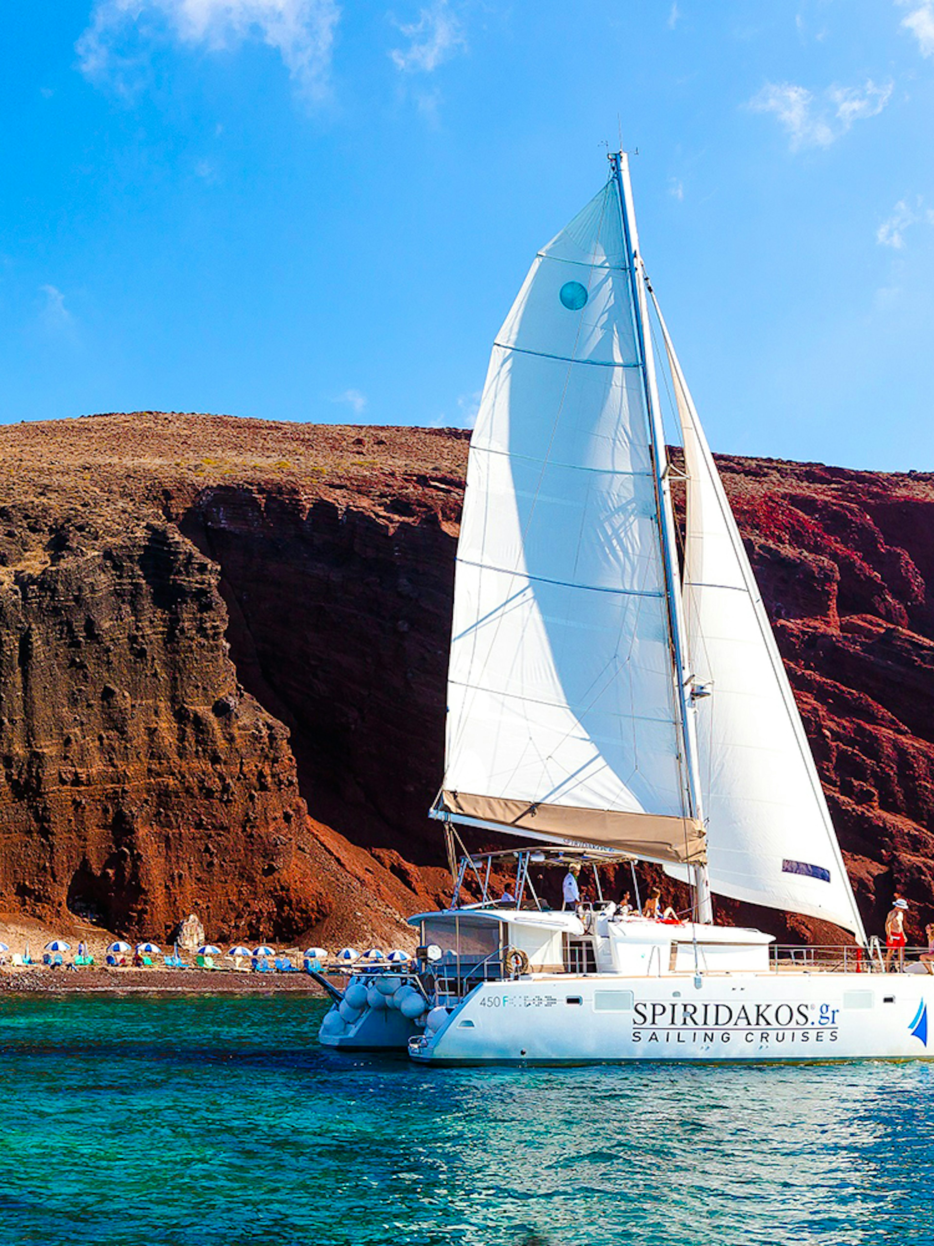Catamaran sailing near the red cliffs of Santorini, Greece.