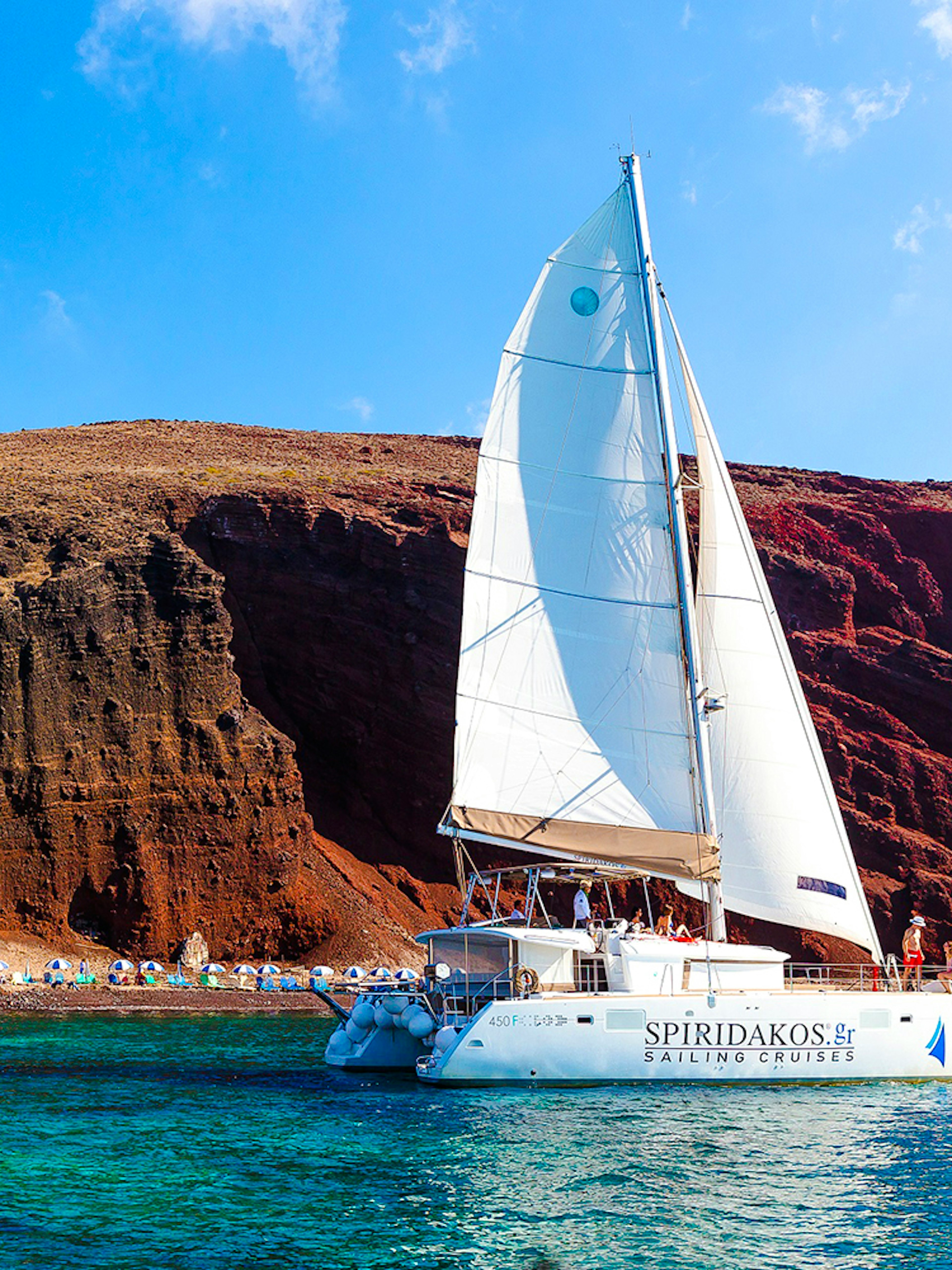 Catamaran sailing near the red cliffs of Santorini, Greece.
