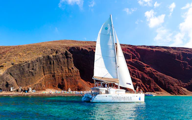 Catamaran sailing near the red cliffs of Santorini, Greece.