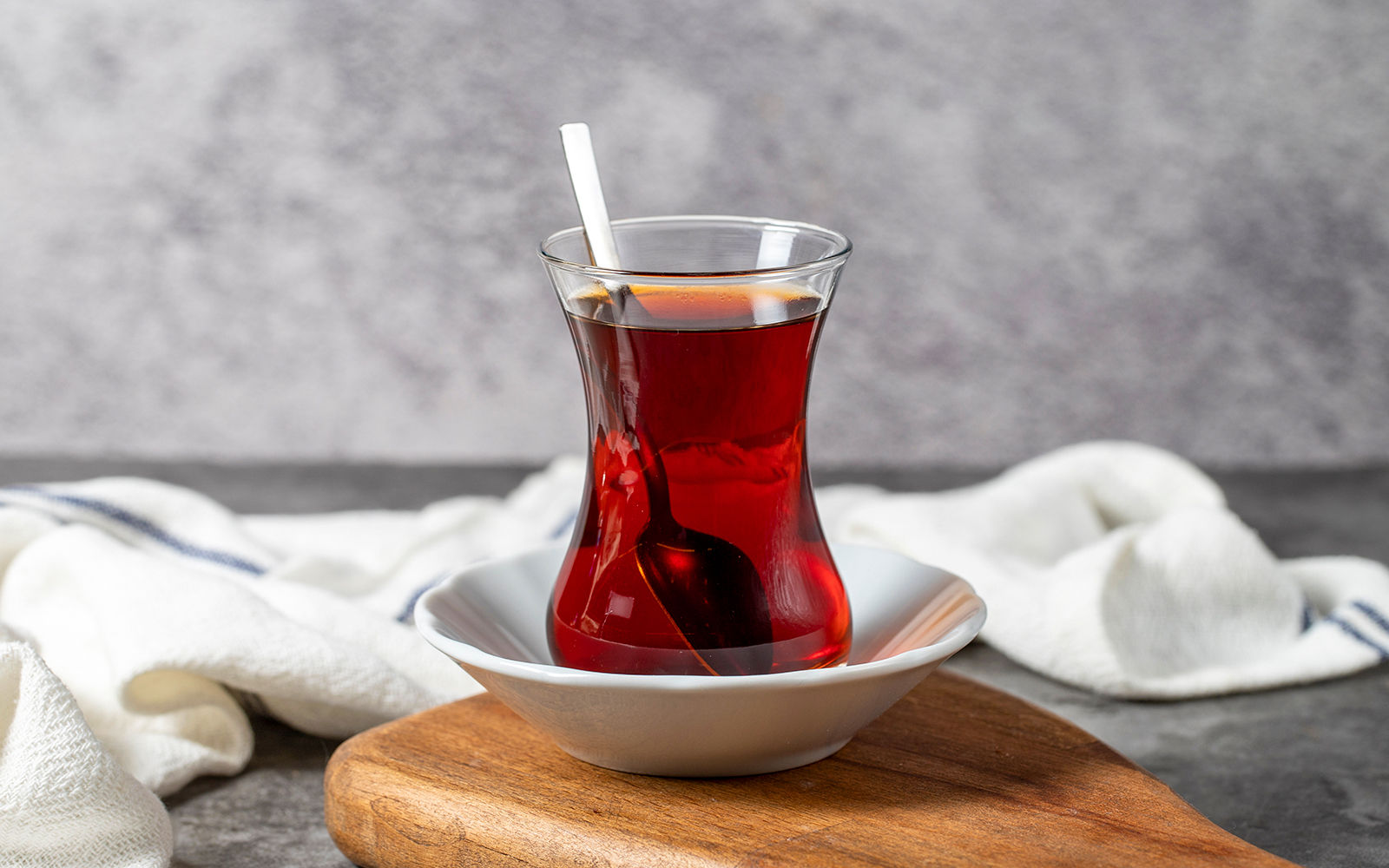 Freshly brewed Turkish tea in a traditional glass with a spoon on a wooden board.