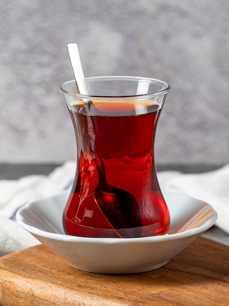 Freshly brewed Turkish tea in a traditional glass with a spoon on a wooden board.
