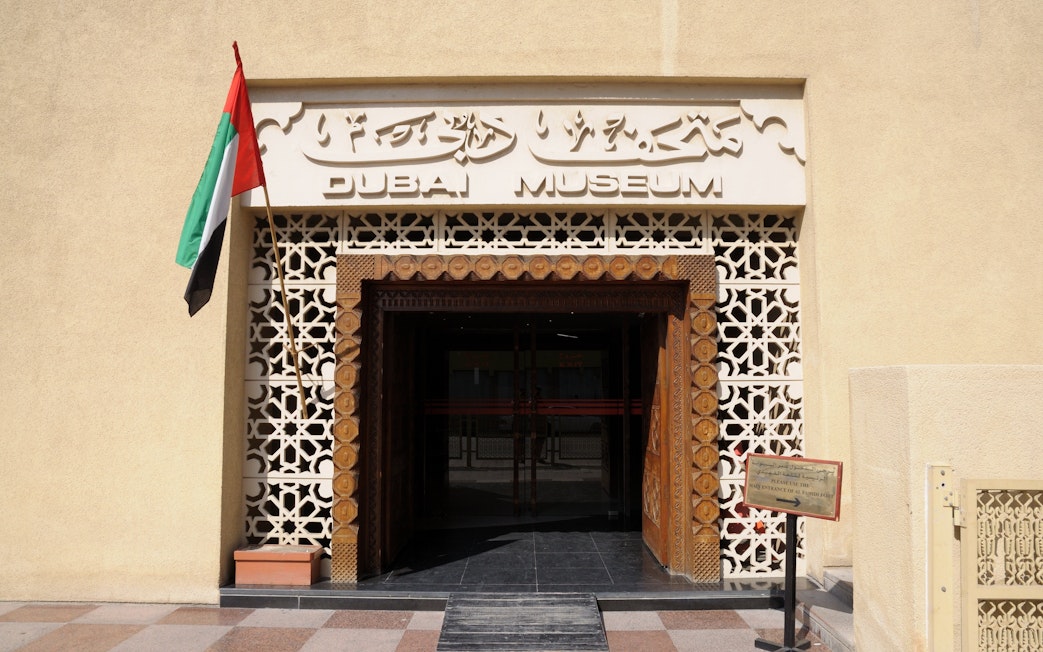 Entrance of Dubai Museum with UAE flag and traditional architectural design.