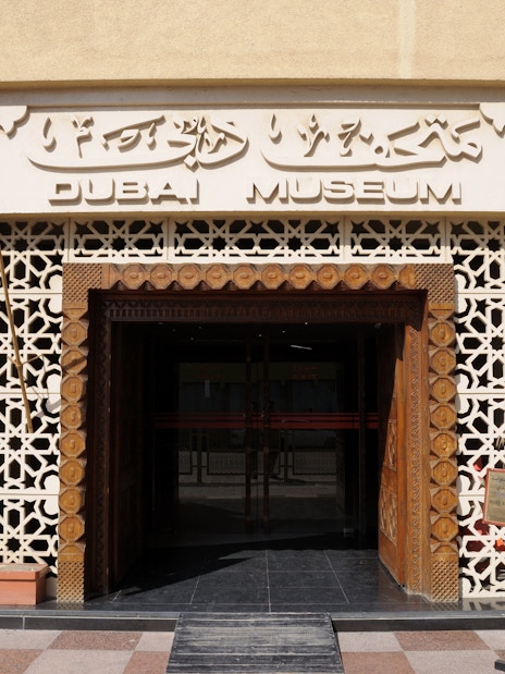 Entrance of Dubai Museum with UAE flag and traditional architectural design.