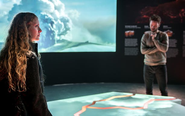 Visitors observing volcanic eruption display at Perlan's Wonders of Iceland exhibit.
