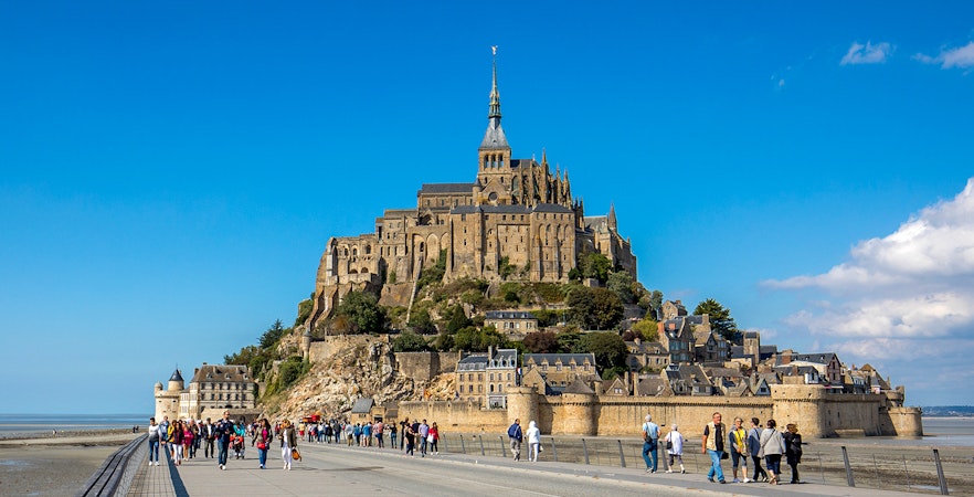Visitors walking towards Mont-Saint-Michel Abbey in Normandy, France.