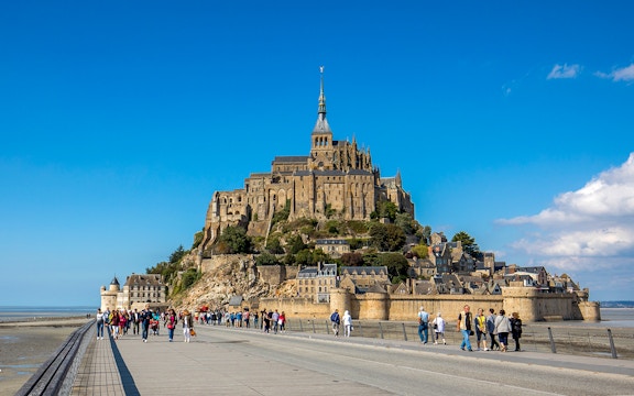 Visitors walking towards Mont-Saint-Michel Abbey in Normandy, France.