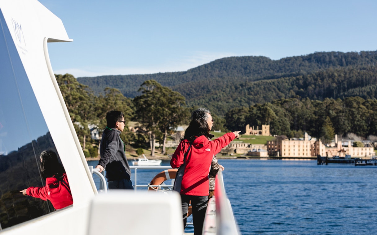 Tourists on a boat pointing towards Port Arthur Historic Site during a harbour cruise in Tasmania.