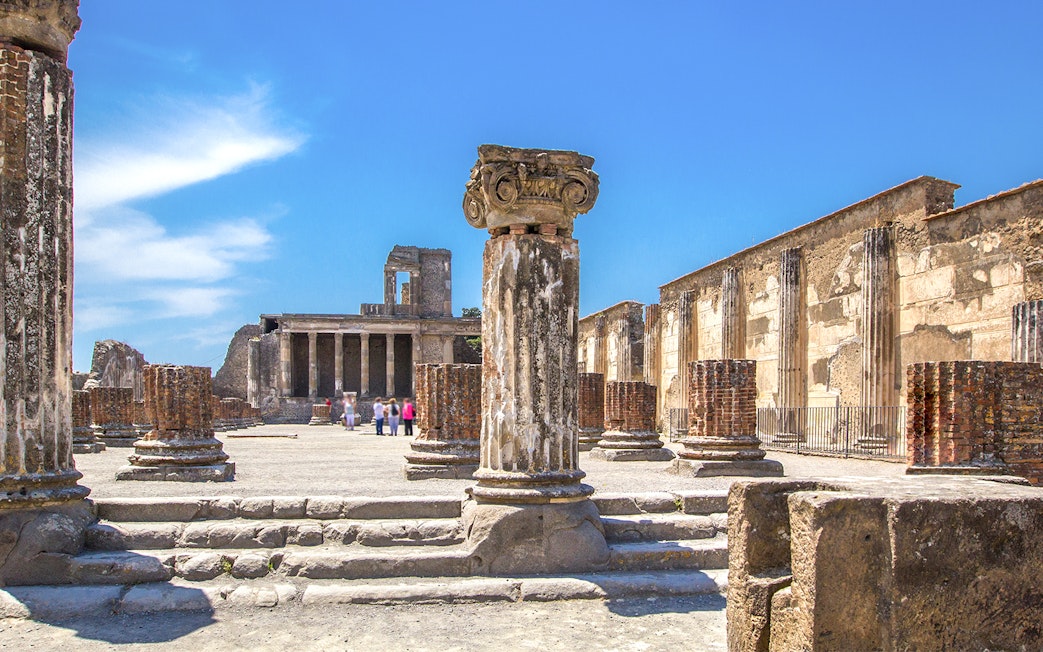 Ancient ruins of Pompeii with columns and Mount Vesuvius in the background.