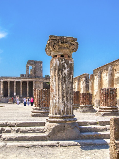 Ancient ruins of Pompeii with columns and Mount Vesuvius in the background.