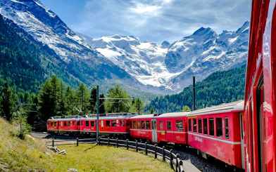 Red train traveling through alpine landscape near Neuschwanstein Castle on a small group day trip.