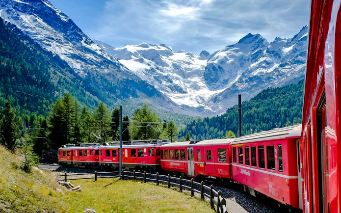 Red train traveling through alpine landscape near Neuschwanstein Castle on a small group day trip.