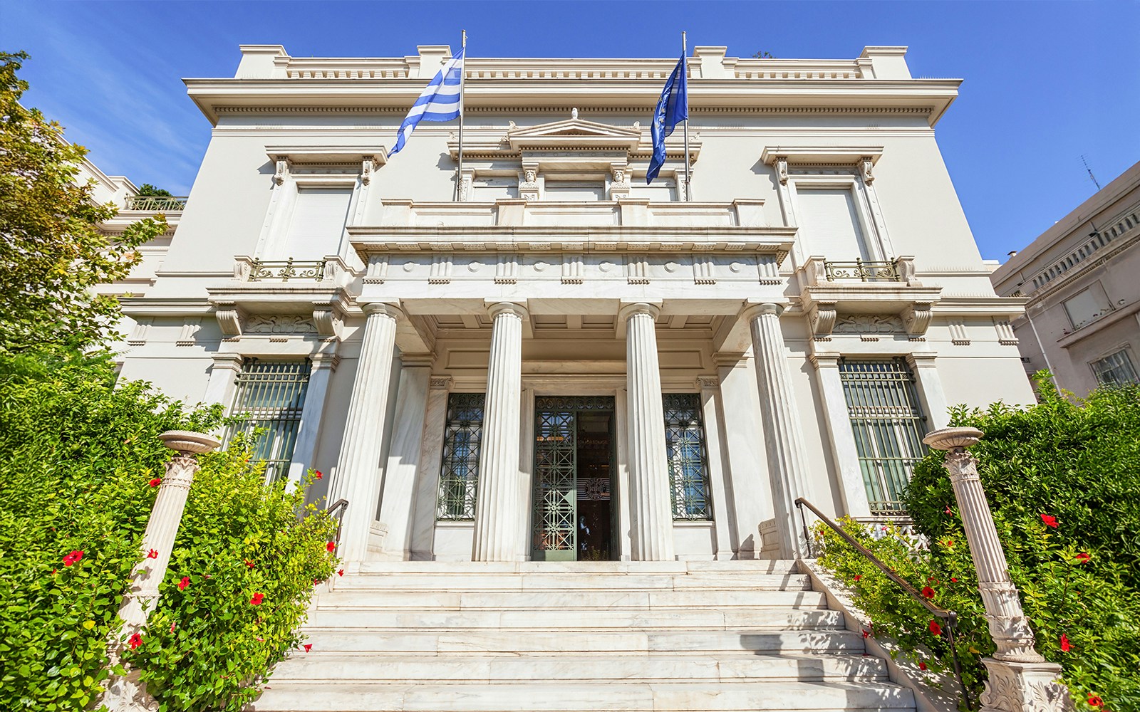 Facade of Benaki Museum in Athens with Greek flags and neoclassical columns.