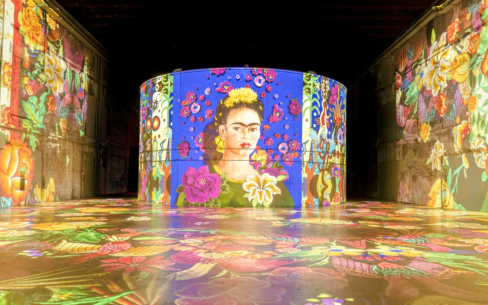 Frida Kahlo artwork projection at Bassins Des Lumieres exhibition, featuring vibrant floral patterns.