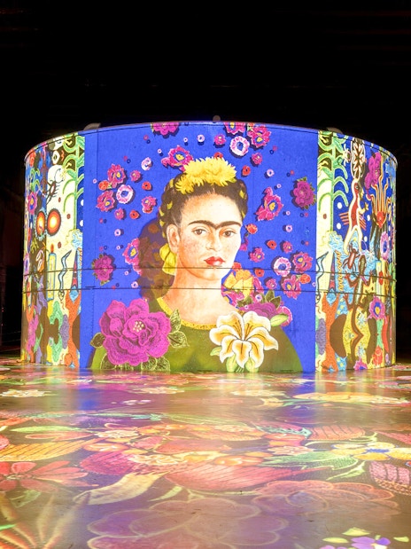 Frida Kahlo artwork projection at Bassins Des Lumieres exhibition, featuring vibrant floral patterns.
