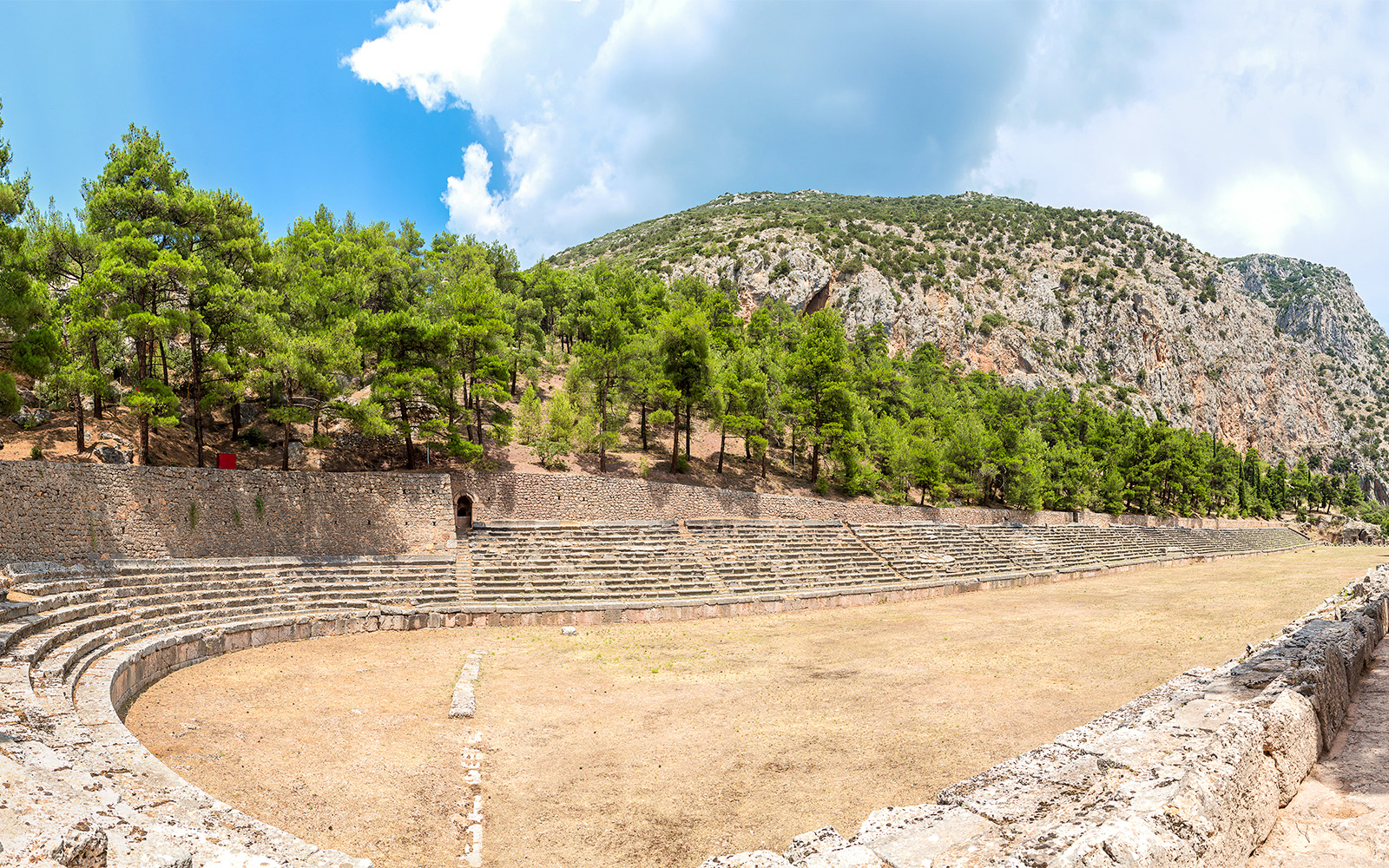 Stadium of Delphi with stone seating and surrounding trees under a clear sky.